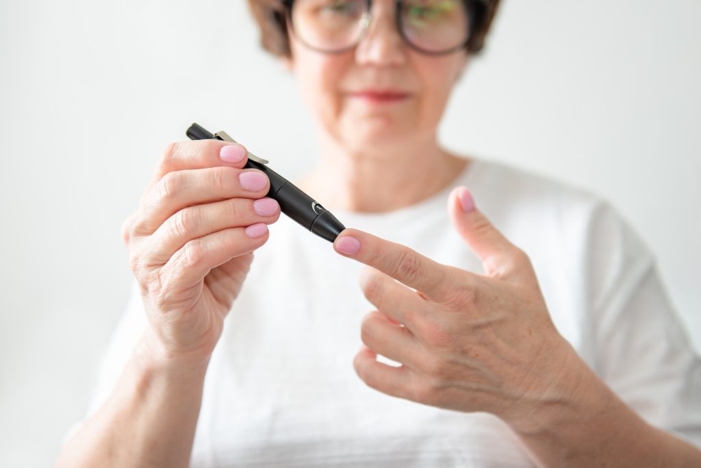 Starija žena vadi krv iz prsta kako bi proverila nivo šećera